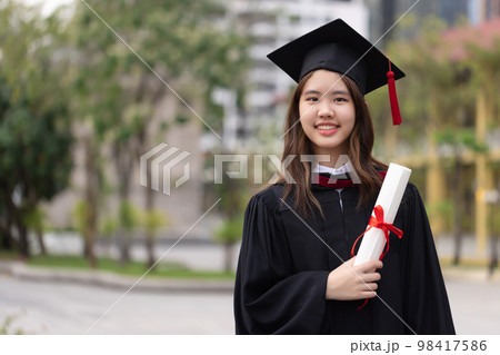 Successful graduation from university. Smiling beautiful Asian girl university or college graduate standing with diploma over university at background. 98417586