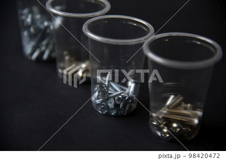 Construction bolts and screws in plastic cups on a black background. Construction accessories. Construction bolts and screws in plastic cups on a black background. Construction accessories. 98420472