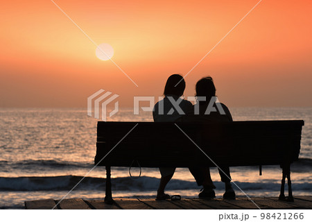 Back view of a couple silhouette, watching sunset on the beach Back view of a couple silhouette, watching sunset on the beach 98421266