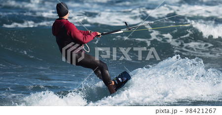 Athletic man jumping on kite surf board on a sea waves. Kiteboarding man among waves quickly goes. Watersport adrenaline fun adventure acitivity Athletic man jumping on kite surf board on a sea waves. Kiteboarding man among waves quickly goes. Watersport adrenaline fun adventure acitivity 98421267