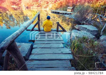 A man sitting on a wooden deck and looking at a forest lake with a granite shore 98421784