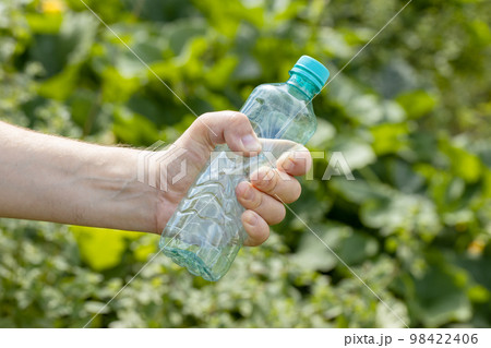 Hand holding crumpled empty plastic bottle in the park Hand holding crumpled empty plastic bottle in the park 98422406