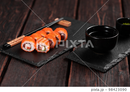 Sushi roll with shrimp and red pepper and tobiko caviar with salad served on black board close-up - Japanese food Sushi roll with shrimp and red pepper and tobiko caviar with salad served on black board close-up - Japanese food 98423090