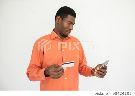 Portrait of happy young man holding credit card and mobile phone Portrait of happy young man holding credit card and mobile phone 98424103