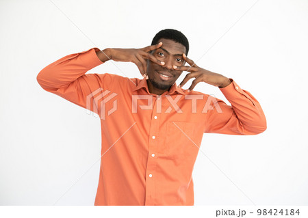 Portrait of happy young man holding fingers at eyes 98424184