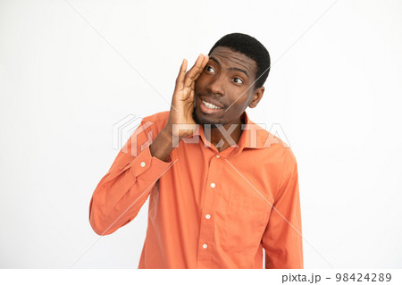 Portrait of happy young man telling gossip covering mouth Portrait of happy young man telling gossip covering mouth 98424289
