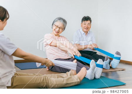 老人ホームでチューブトレーニング・リハビリするシニア・高齢者の男女と理学療法士・介護士・トレーナー 98427005