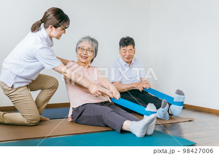 老人ホームでチューブトレーニング・リハビリするシニア・高齢者の男女と理学療法士・介護士・トレーナー 98427006