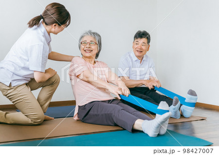 老人ホームでチューブトレーニング・リハビリするシニア・高齢者の男女と理学療法士・介護士・トレーナー 98427007