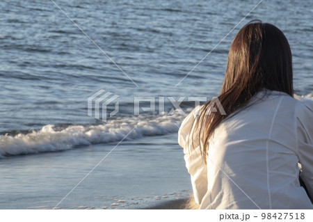 夕暮れの海岸で黄昏る女性の後ろ姿 98427518