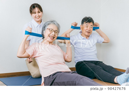 老人ホームでチューブトレーニング・リハビリするシニア・高齢者の男女と理学療法士・介護士・トレーナー 老人ホームでチューブトレーニング・リハビリするシニア・高齢者の男女と理学療法士・介護士・トレーナー 98427676