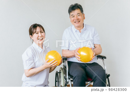 老人ホームでボール体操・運動・リハビリするシニア・高齢者の男性と理学療法士・介護士・トレーナー 98428300