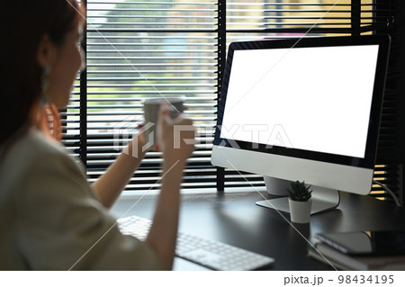 Computer monitor view over female shoulder, businesswoman holding coffee cup and reading email on computer 98434195