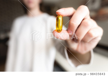 woman's hand holds an Omega-3 capsule against the background of herself in a white sweater, the background is in blur. Useful fish oil capsule tablets 98435643