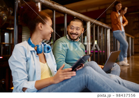 Diverse coworkers sitting on floor talking while using digital tablets 98437556