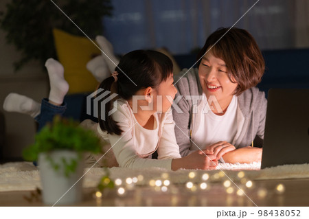 夜リビングで寝転がってパソコンを見る小学生の女の子とママ 98438052