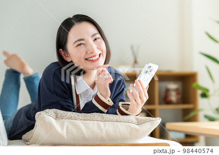 リビングでスマホを見る若い女性 98440574