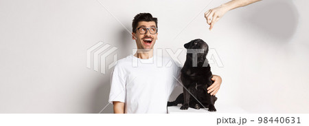 Amazed young man in glasses hugging his dog, pet owner and pug staring at upper left corner promo offer, standing over white background 98440631