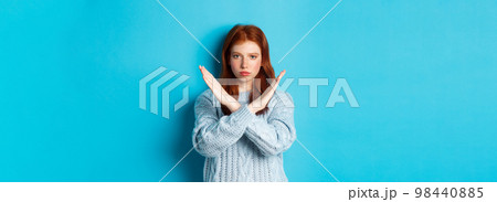 Serious redhead girl looking confident, showing cross gesture to stop and forbid action, standing over blue background 98440885
