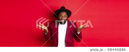 Clueless and unbothered Black man shrugging with indifferent look, dont care, standing against red background Clueless and unbothered Black man shrugging with indifferent look, dont care, standing against red background 98440886