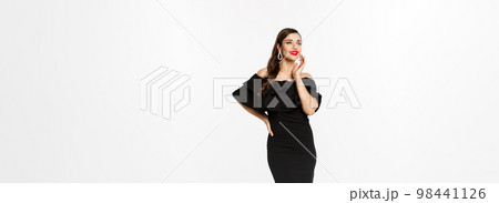 Vertical shot of attractive woman standing in elegant black dress with christmas gifts, smiling happy, standing over white background 98441126