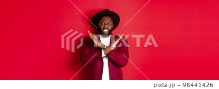 Angry Black man showing cross to stop something, looking furious and declining offer, standing in party clothes, red background Angry Black man showing cross to stop something, looking furious and declining offer, standing in party clothes, red background 98441426