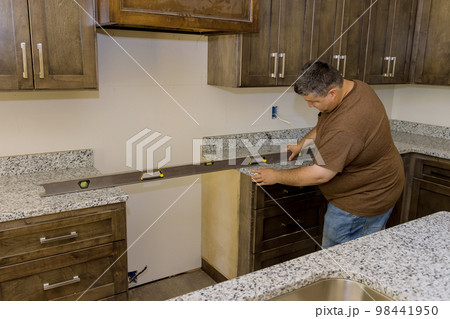 During installation of new kitchen cabinet set worker hangs level to ensure cabinets are level 98441950
