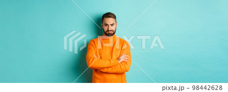 Silly sad guy with beard, sulking and looking offended, cross arms on chest and frowning upset, standing over light blue background Silly sad guy with beard, sulking and looking offended, cross arms on chest and frowning upset, standing over light blue background 98442628