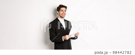 Image of handsome businessman in suit, holding documents and smiling, standing against white background Image of handsome businessman in suit, holding documents and smiling, standing against white background 98442782