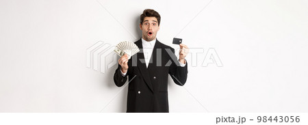 Portrait of surprised handsome man i suit, showing credit card with money, standing against white background Portrait of surprised handsome man i suit, showing credit card with money, standing against white background 98443056