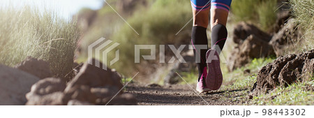 Trail running athlete exercising for fitness and health outdoors on mountain pathway, closeup of running shoes in action Trail running athlete exercising for fitness and health outdoors on mountain pathway, closeup of running shoes in action 98443302