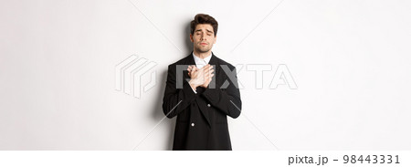 Portrait of dreamy and heartfelt bearded man in suit, close eyes and hold hands on heart, remember something, standing nostalgic over white background Portrait of dreamy and heartfelt bearded man in suit, close eyes and hold hands on heart, remember something, standing nostalgic over white background 98443331