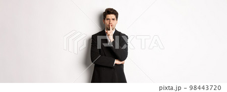 Portrait of angry boss in suit shushing at you, telling to be quiet, showing taboo hush sign and frowning, standing over white background Portrait of angry boss in suit shushing at you, telling to be quiet, showing taboo hush sign and frowning, standing over white background 98443720