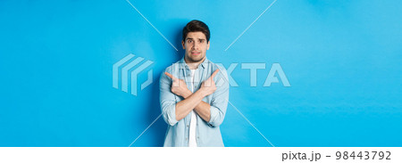 Portrait of nervous guy pointing fingers sideways, looking indecisive and asking for help with choice, showing left and right promo offers, standing against blue background 98443792