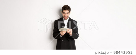 Image of excited handsome businessman, counting money and smiling amused, standing against white background in suit 98443953