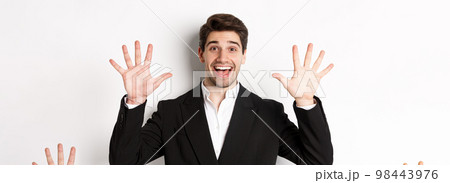 Close-up of handsome businessman in black suit, smiling amazed, showing number ten, standing over white background Close-up of handsome businessman in black suit, smiling amazed, showing number ten, standing over white background 98443976