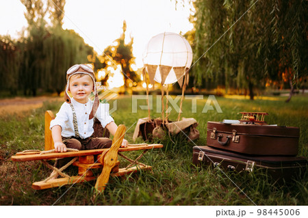 Cute little pilot boy in vintage aviator hat looking at camera while sitting on big toy wooden plane Cute little pilot boy in vintage aviator hat looking at camera while sitting on big toy wooden plane 98445006