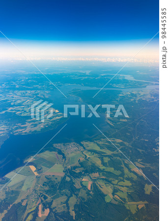 Aerial view from airplane window above green ground. View from the airplane window with beautiful clouds at sunrise Aerial view from airplane window above green ground. View from the airplane window with beautiful clouds at sunrise 98445585