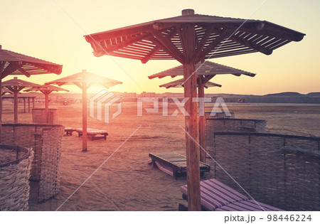 Silhouettes of beach sun umbrellas, beds and windscreens at sunset, color toning applied. Silhouettes of beach sun umbrellas, beds and windscreens at sunset, color toning applied. 98446224