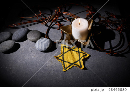 Holocaust memory day. Barbed wire, stones, yellow star and burning candle on black background 98446880