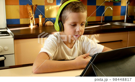 A boy old in headphones looks at the tablet and says something in response. Online learning 98448817