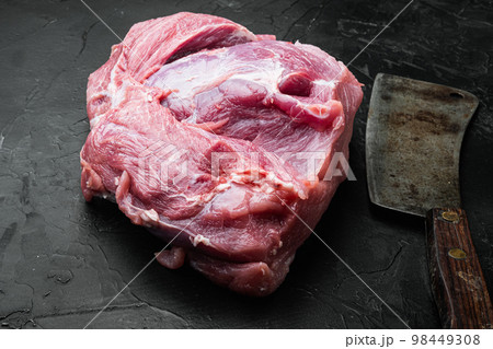 Pork meat shoulder , with old butcher cleaver knife, on black dark stone table background Pork meat shoulder , with old butcher cleaver knife, on black dark stone table background 98449308