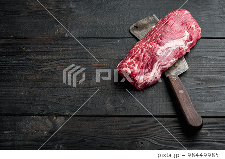 Beef fillet mignon cut raw , with old butcher cleaver knife, on black wooden table background, with copy space for text 98449985
