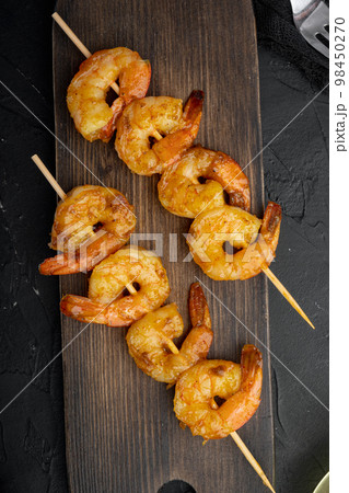 Roasted peeled prawn with skewer, on wooden serving board, on black background, top view flat lay Roasted peeled prawn with skewer, on wooden serving board, on black background, top view flat lay 98450270
