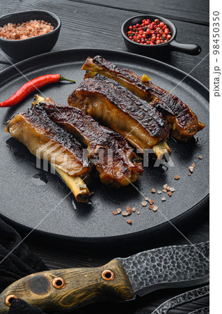 Grilled barbecue pork ribs, on plate, with barbeque knife and meat fork, on black wooden table background 98450350