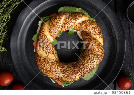 Simit bagel sandwich with lettuce, tomato, cheese, on black wooden table background, top view flat lay Simit bagel sandwich with lettuce, tomato, cheese, on black wooden table background, top view flat lay 98450361