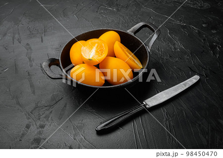 Yellow whole tomato with a slice, on black dark stone table background Yellow whole tomato with a slice, on black dark stone table background 98450470