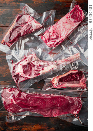 Vacuum packed organic raw beef classic cuts, tomahawk, t bone, club steak, rib eye and tenderloin cuts, on old dark wooden table background Vacuum packed organic raw beef classic cuts, tomahawk, t bone, club steak, rib eye and tenderloin cuts, on old dark wooden table background 98450481