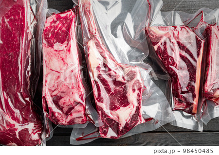 Beef steak vacuum, tomahawk, t bone, club steak, rib eye and tenderloin cuts, on black wooden table background, top view flat lay Beef steak vacuum, tomahawk, t bone, club steak, rib eye and tenderloin cuts, on black wooden table background, top view flat lay 98450485