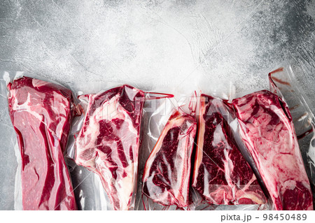 Raw marbled beef steak in vacuum packaging, tomahawk, t bone, club steak, rib eye and tenderloin cuts, on gray stone background, top view flat lay, with copy space for text Raw marbled beef steak in vacuum packaging, tomahawk, t bone, club steak, rib eye and tenderloin cuts, on gray stone background, top view flat lay, with copy space for text 98450489